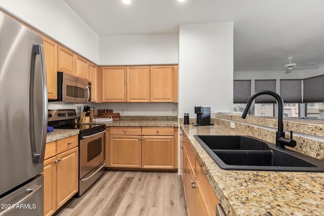 kitchen with stainless steel appliances, light brown cabinets, light stone countertops, sink, and light hardwood / wood-style flooring