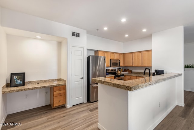 kitchen featuring kitchen peninsula, light hardwood / wood-style flooring, light stone countertops, appliances with stainless steel finishes, and built in desk