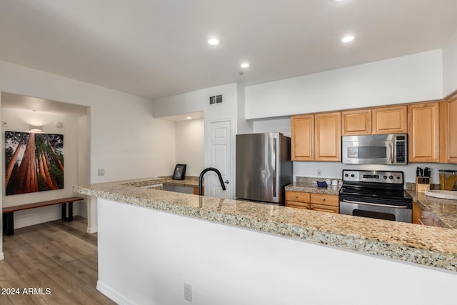 kitchen featuring stainless steel appliances, sink, kitchen peninsula, light stone counters, and wood-type flooring