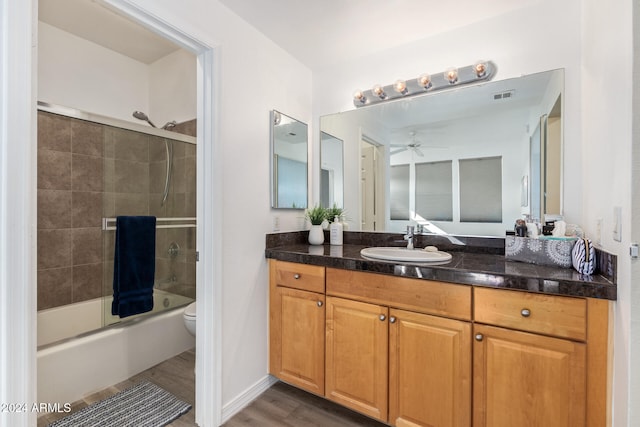 full bathroom with vanity, hardwood / wood-style floors, toilet, combined bath / shower with glass door, and ceiling fan