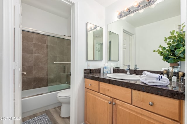 full bathroom with hardwood / wood-style floors, bath / shower combo with glass door, vanity, and toilet