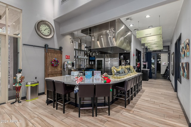 kitchen featuring light wood-type flooring, a barn door, a breakfast bar, and light stone countertops