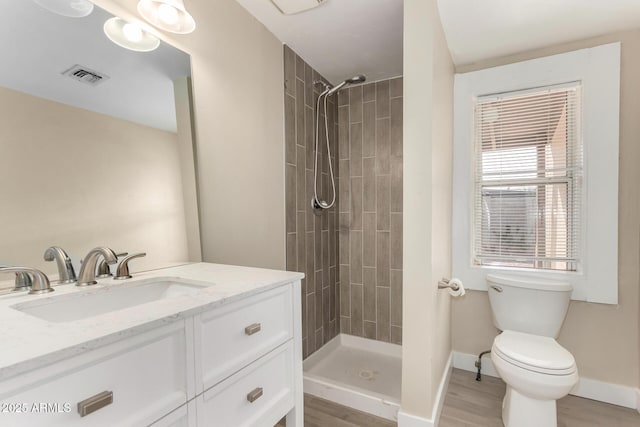 bathroom featuring a tile shower, hardwood / wood-style floors, vanity, and toilet