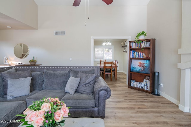 living room featuring ceiling fan, light hardwood / wood-style floors, and a towering ceiling