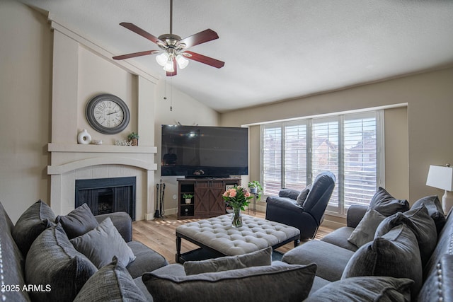 living room featuring vaulted ceiling, a textured ceiling, hardwood / wood-style flooring, ceiling fan, and a fireplace