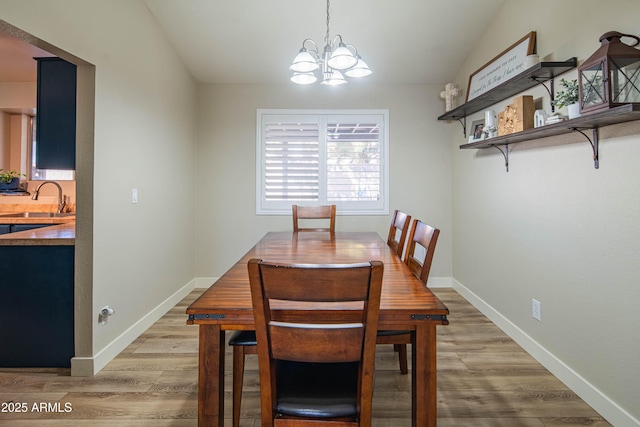 dining area featuring an inviting chandelier, sink, lofted ceiling, and light wood-type flooring