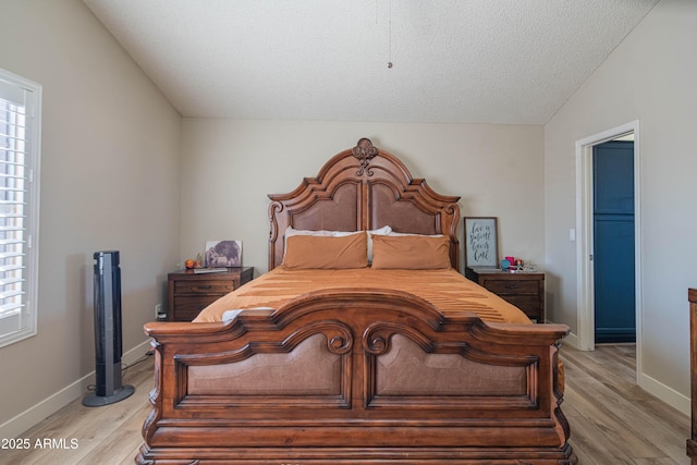 bedroom featuring vaulted ceiling, light hardwood / wood-style floors, and a textured ceiling