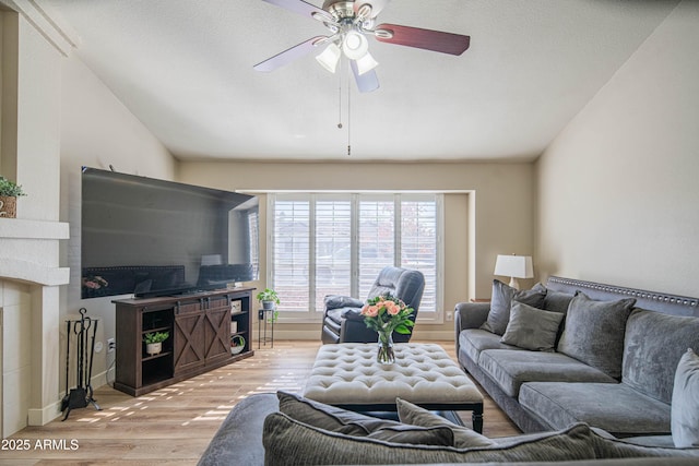 living room with a fireplace, lofted ceiling, light wood-type flooring, ceiling fan, and a textured ceiling