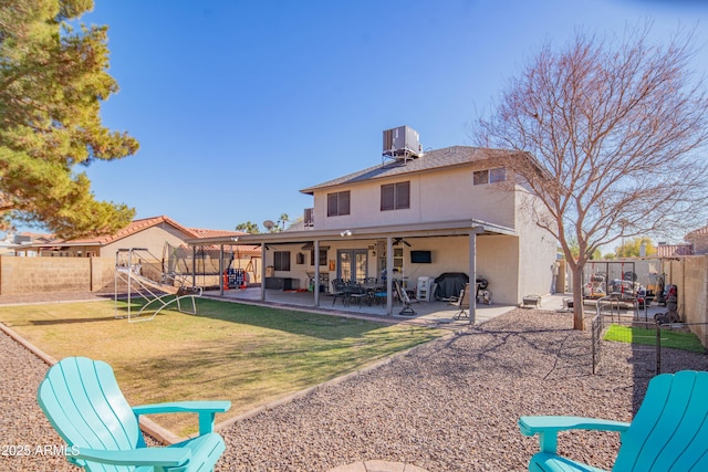 back of property with ceiling fan, a trampoline, a yard, a patio, and central AC unit