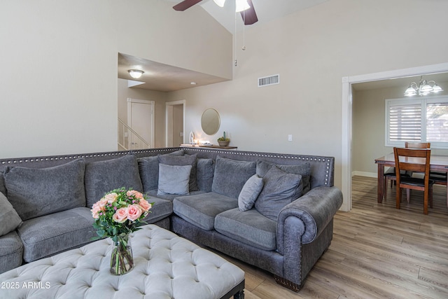 living room with ceiling fan with notable chandelier, light hardwood / wood-style flooring, and high vaulted ceiling