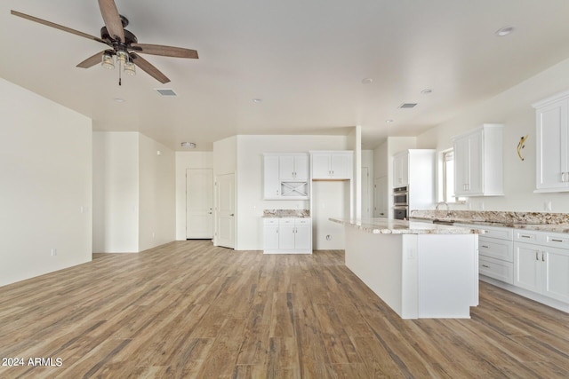 kitchen with visible vents, white cabinets, a kitchen island, light stone countertops, and light wood-style floors