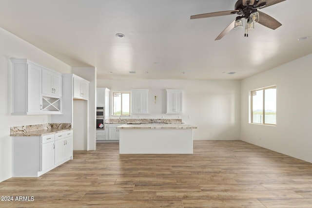 kitchen with white cabinets, a kitchen island, light wood finished floors, and light stone countertops