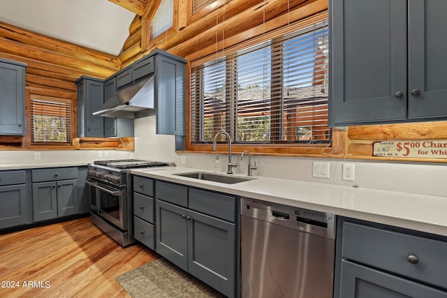 kitchen with appliances with stainless steel finishes, light wood-type flooring, wall chimney range hood, log walls, and lofted ceiling with beams