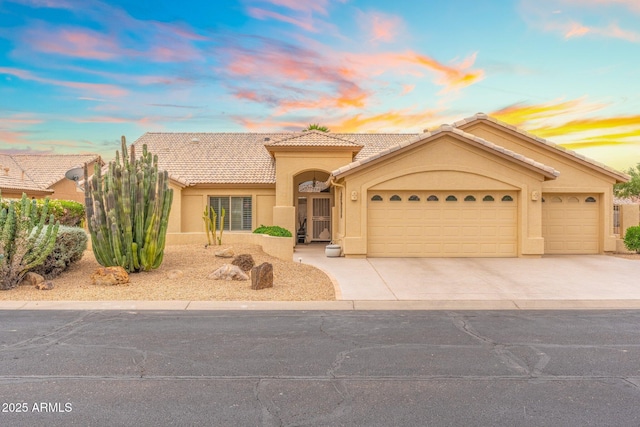 mediterranean / spanish home with a garage, driveway, a tile roof, and stucco siding
