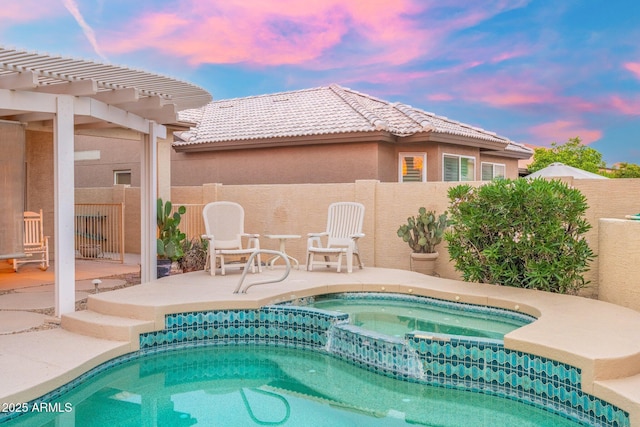 pool at dusk with a pool with connected hot tub, fence, and a patio area