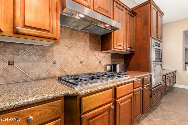 kitchen featuring backsplash, brown cabinets, under cabinet range hood, and stainless steel appliances