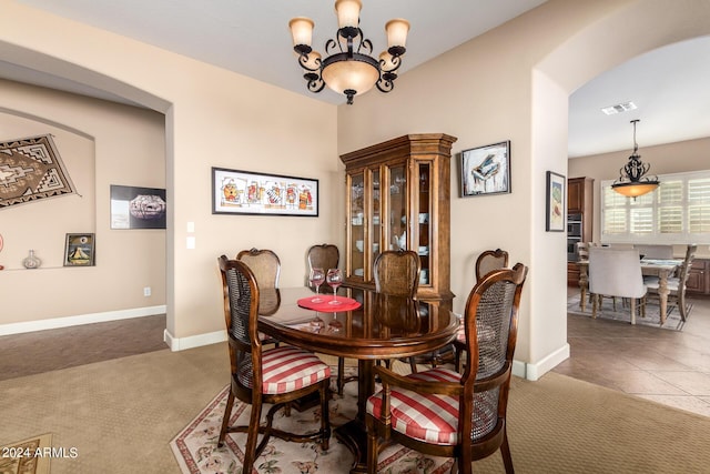 carpeted dining space featuring tile patterned flooring, visible vents, baseboards, a chandelier, and arched walkways