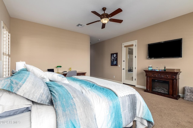 carpeted bedroom with a glass covered fireplace, a ceiling fan, visible vents, and baseboards