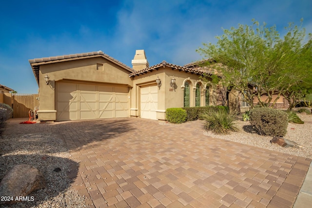 mediterranean / spanish home with decorative driveway, a tile roof, an attached garage, and stucco siding