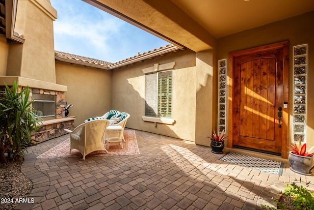 doorway to property featuring a tile roof, stucco siding, an outdoor stone fireplace, a patio area, and stone siding