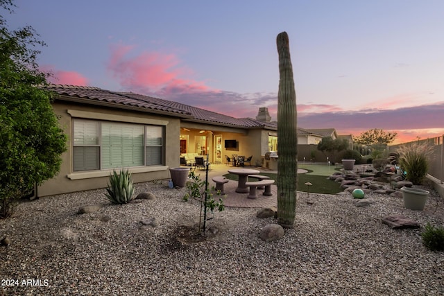 back of house at dusk with stucco siding, fence, a tile roof, and a patio area