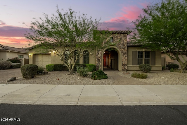 mediterranean / spanish home featuring an attached garage, stucco siding, stone siding, a tiled roof, and decorative driveway