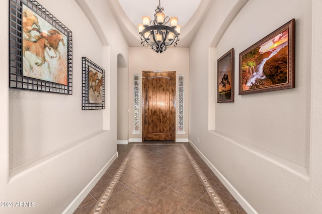 doorway with arched walkways, an inviting chandelier, dark tile patterned floors, and baseboards