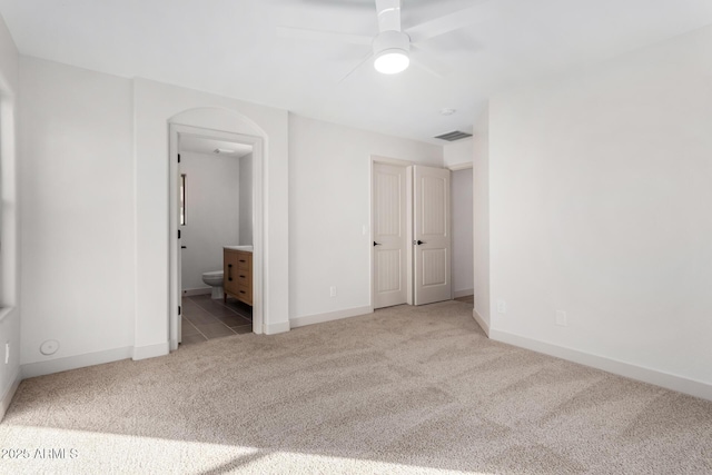 unfurnished bedroom with ceiling fan, ensuite bathroom, and light colored carpet