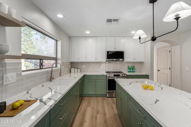 kitchen with green cabinets, appliances with stainless steel finishes, decorative light fixtures, white cabinetry, and light hardwood / wood-style floors