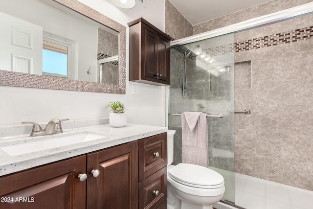 bathroom featuring toilet, vanity, and a shower with shower door