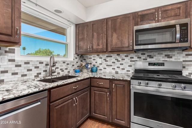 kitchen featuring dark brown cabinetry, sink, stainless steel appliances, light stone countertops, and decorative backsplash