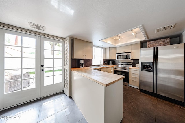 6533 N 10th Pl, Phoenix, AZ 85014 - kitchen with appliances with stainless steel finishes, a tray ceiling, a peninsula, dark tile patterned floors, and french doors