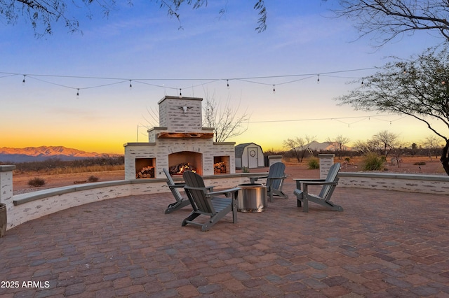 patio terrace at dusk featuring an outdoor brick fireplace and a mountain view