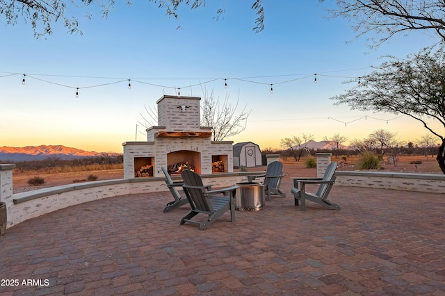 patio terrace at dusk with an outdoor brick fireplace and a mountain view