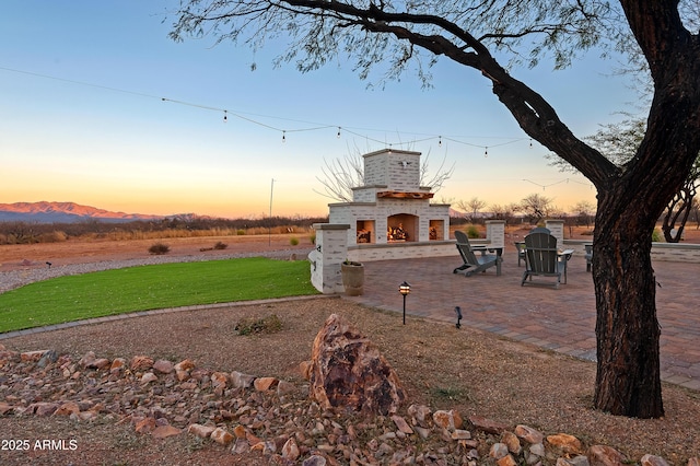 yard at dusk with exterior fireplace, a mountain view, and a patio