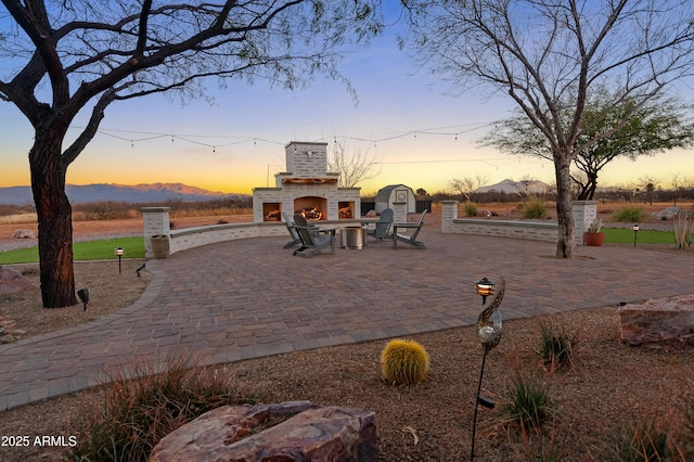 patio terrace at dusk featuring an outdoor brick fireplace and a mountain view