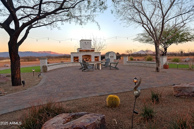 patio terrace at dusk with exterior fireplace and a mountain view