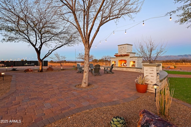 patio terrace at dusk featuring an outdoor brick fireplace and a mountain view