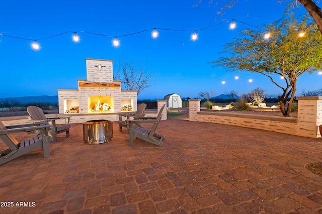 patio terrace at dusk with a storage shed and a fireplace