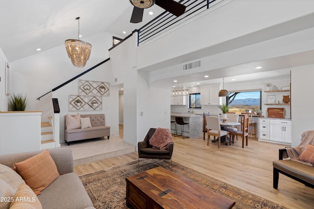 living room with ceiling fan with notable chandelier, high vaulted ceiling, and light wood-type flooring