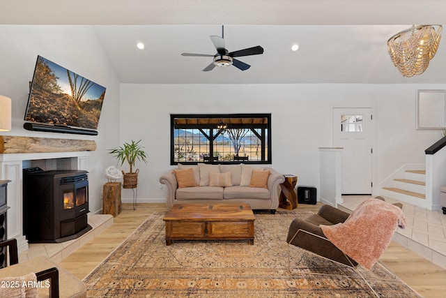 living room featuring vaulted ceiling, a wood stove, ceiling fan, and light wood-type flooring