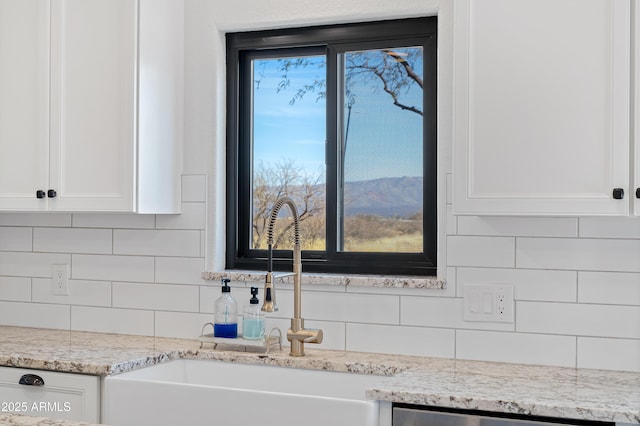 kitchen featuring sink, light stone counters, tasteful backsplash, a mountain view, and white cabinets