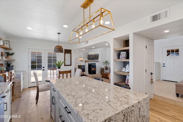 kitchen featuring french doors, a center island, light stone counters, and decorative light fixtures