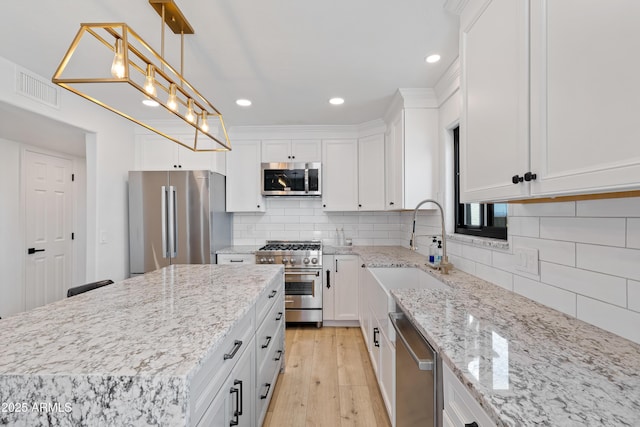 kitchen with sink, white cabinetry, stainless steel appliances, light stone countertops, and decorative light fixtures