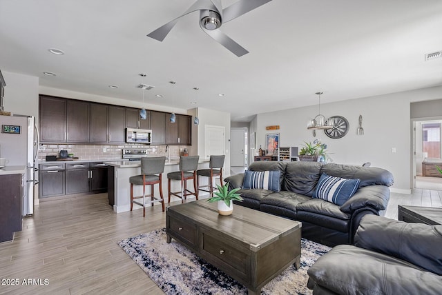 living room with recessed lighting, visible vents, light wood finished floors, and ceiling fan with notable chandelier