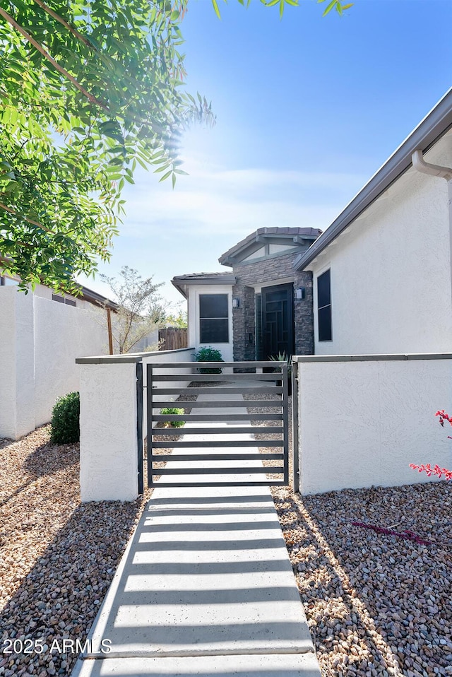 view of front of property with a fenced front yard, a gate, stone siding, and stucco siding