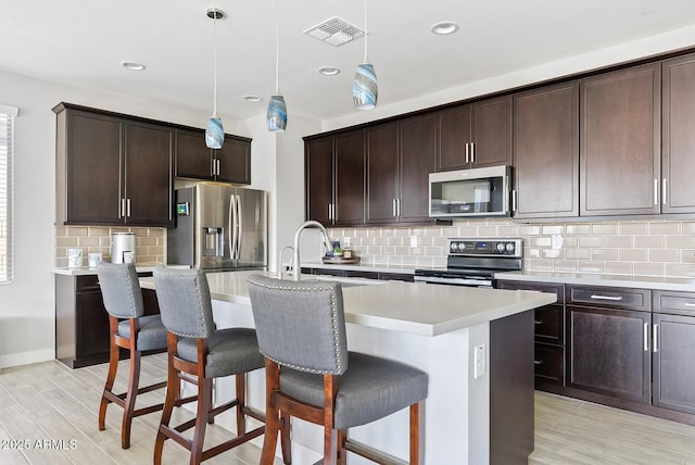 kitchen featuring visible vents, light wood-type flooring, a breakfast bar, and stainless steel appliances