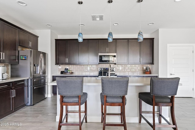 kitchen with light wood finished floors, dark brown cabinetry, a kitchen bar, and stainless steel appliances