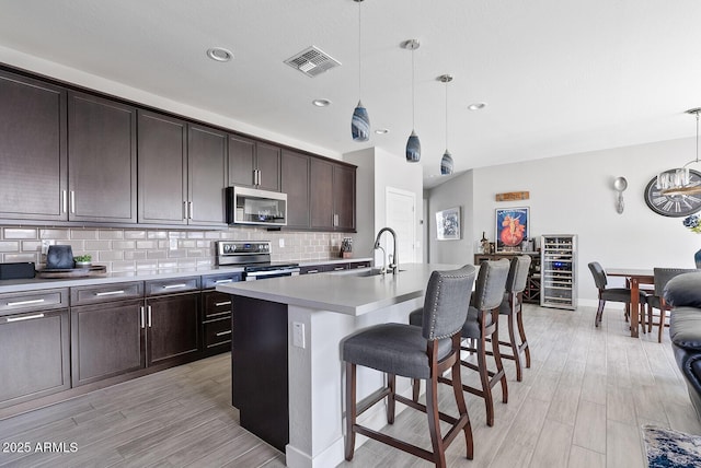 kitchen featuring decorative backsplash, dark brown cabinetry, a breakfast bar, a sink, and stainless steel appliances