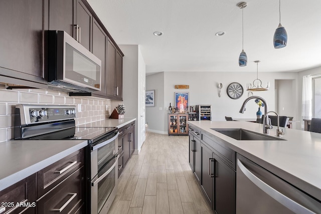 kitchen with pendant lighting, appliances with stainless steel finishes, tasteful backsplash, a sink, and light countertops
